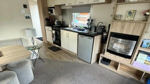 A compact kitchen with a stove, microwave, and oven, a small dining area with a table and chairs, and a bookshelf with various items. - Highland Chalet Retreat in Boat of Garten (Boat of Garten)