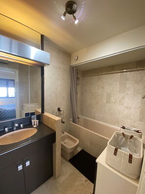 A modern bathroom with a large mirror, a bathtub, a toilet, and a vanity with a sink.