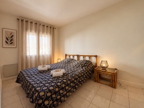 A bedroom with a bed, a bedside table with a lamp, and a window with curtains.