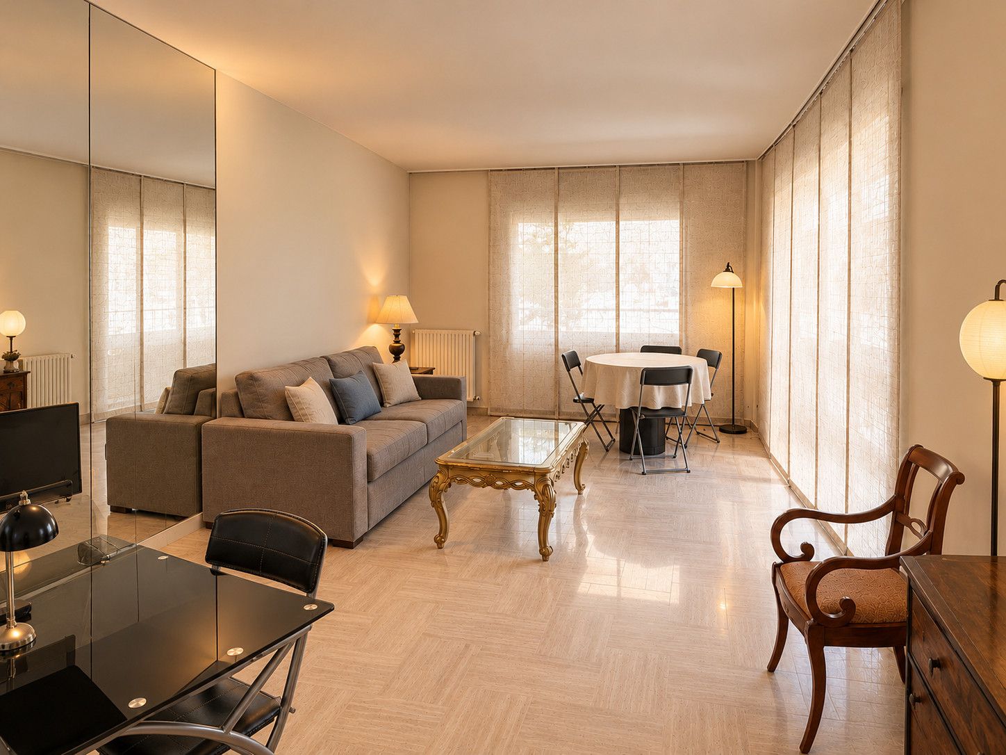 A modern living room with a sofa, a glass coffee table, a dining table with chairs, and a lamp.
