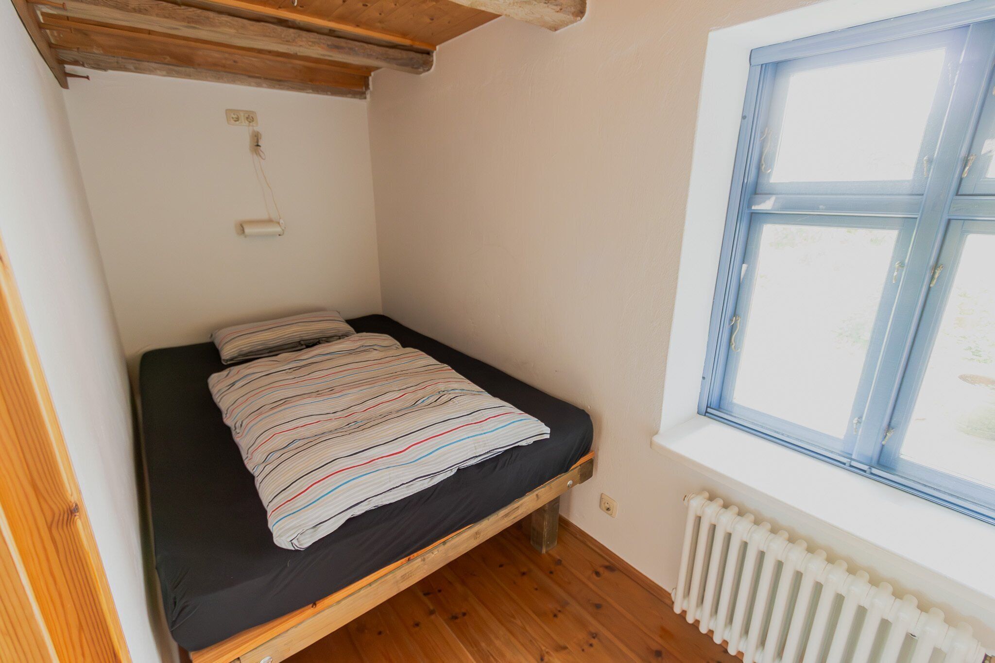 Une petite chambre avec un lit simple, un plancher en bois, une fenêtre donnant sur un paysage agréable et un radiateur.