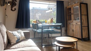 Ett mysigt vardagsrum med en soffa, ett matbord med stolar, ett träskåp och en vacker utsikt genom ett stort fönster.