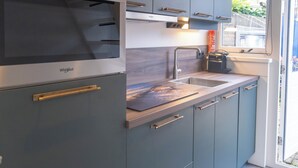Ett modernt kök med en inbyggd mikrovågsugn, en diskho i rostfritt stål och ett fönster med utsikt över en trädgård.