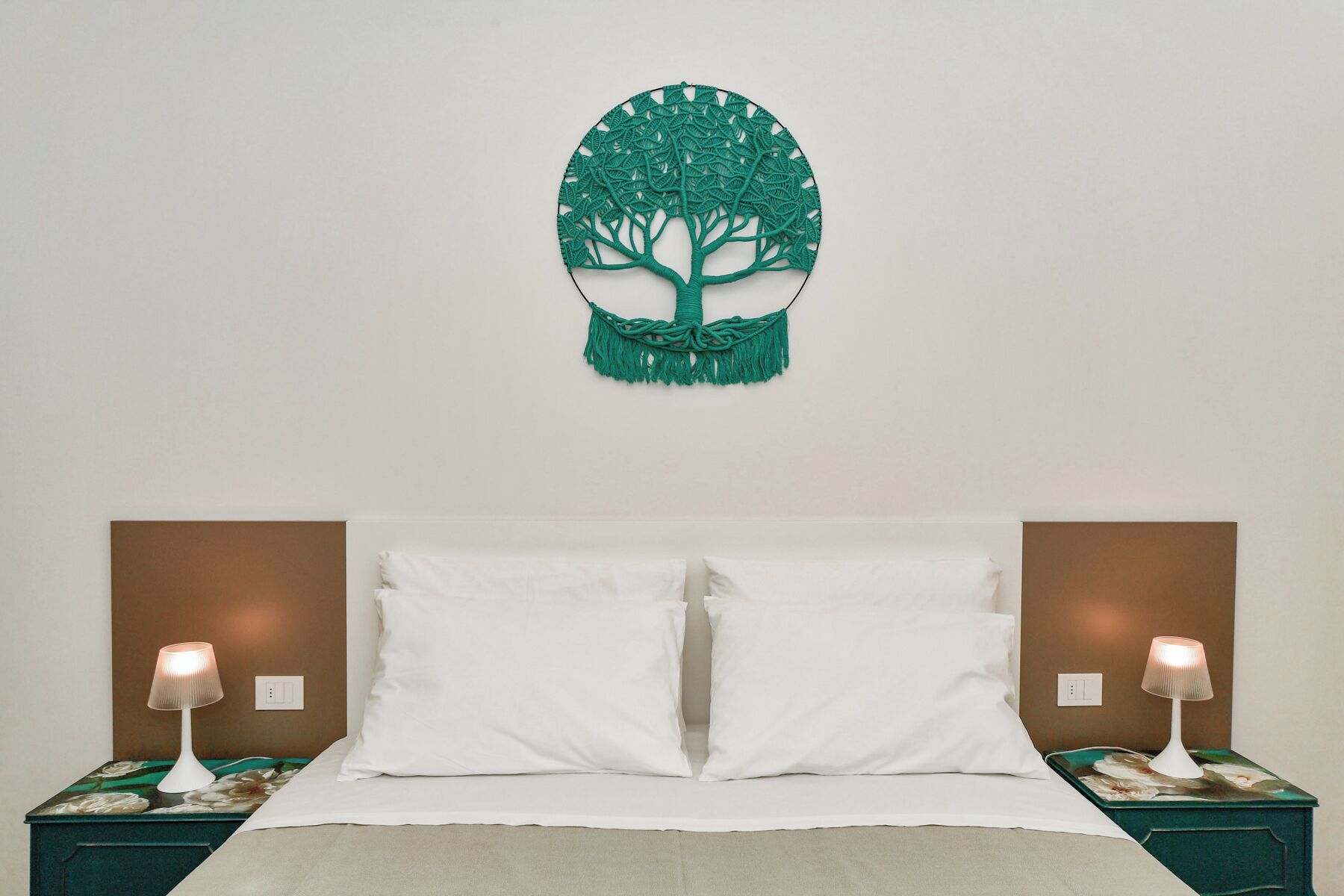A bed with white linens, two bedside tables with lamps, and a wall-mounted tree decoration.