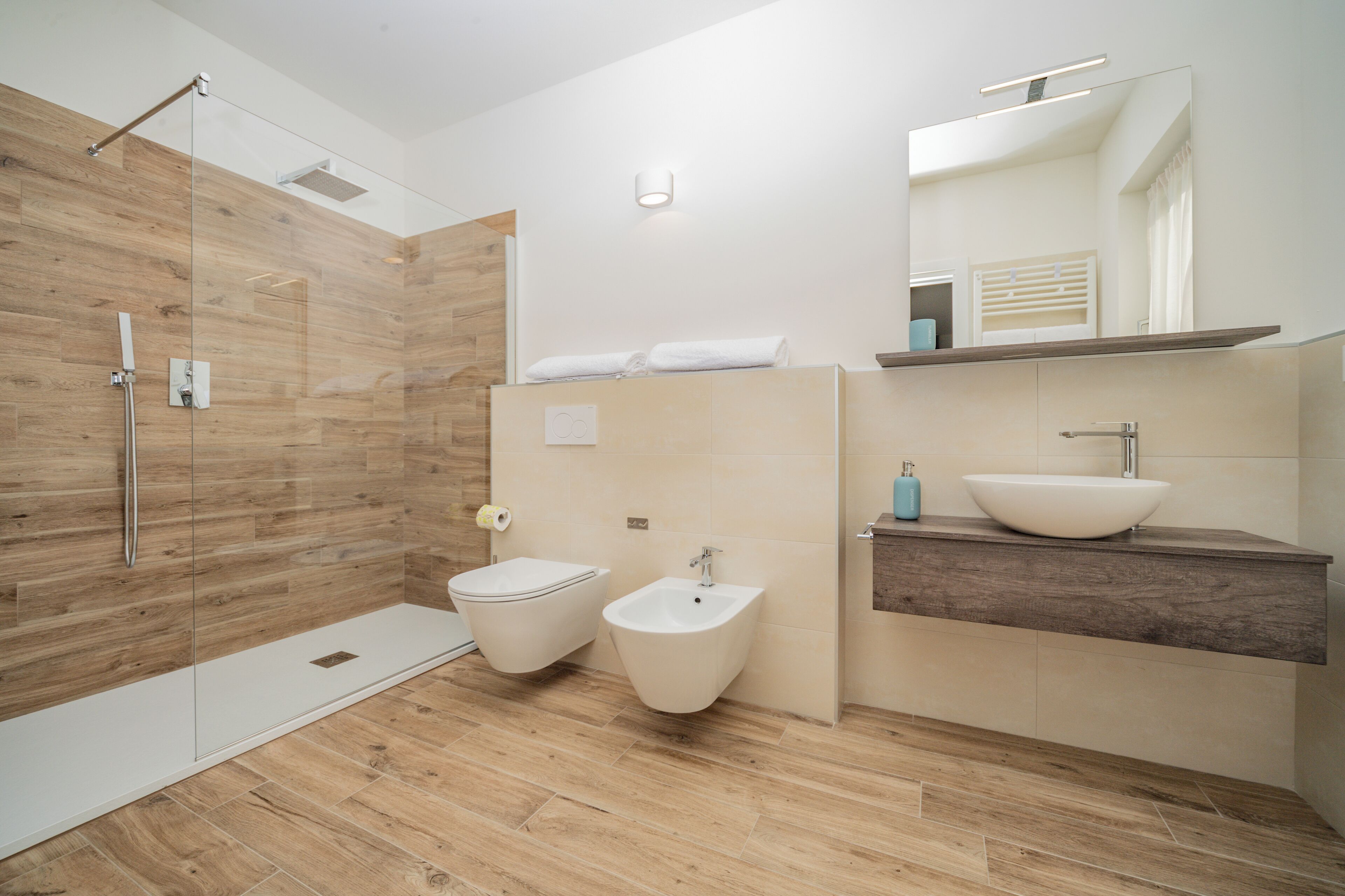 A modern bathroom with a wooden shower enclosure, a bidet, a sink, and a mirror above the vanity.