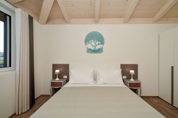 Un dormitorio con una cama, dos mesitas de noche, un adorno de árbol de macramé en la pared y una ventana con cortinas.