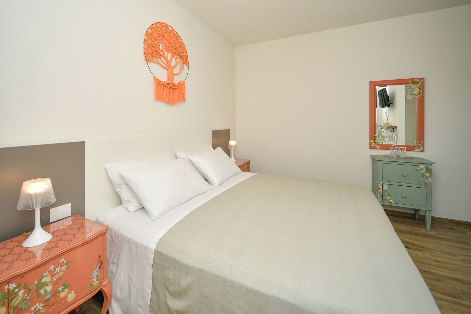 A bedroom with a bed, bedside lamps, a dresser, a mirror, and a wall decoration.