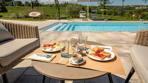 An outdoor dining area with wicker furniture, a table with plates of food, a pitcher, and glasses. - Tenuta Cà Bassa (Castel San Pietro Terme)