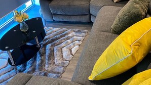 A modern living room with a grey sectional sofa, yellow cushions, a black coffee table, and a patterned rug.