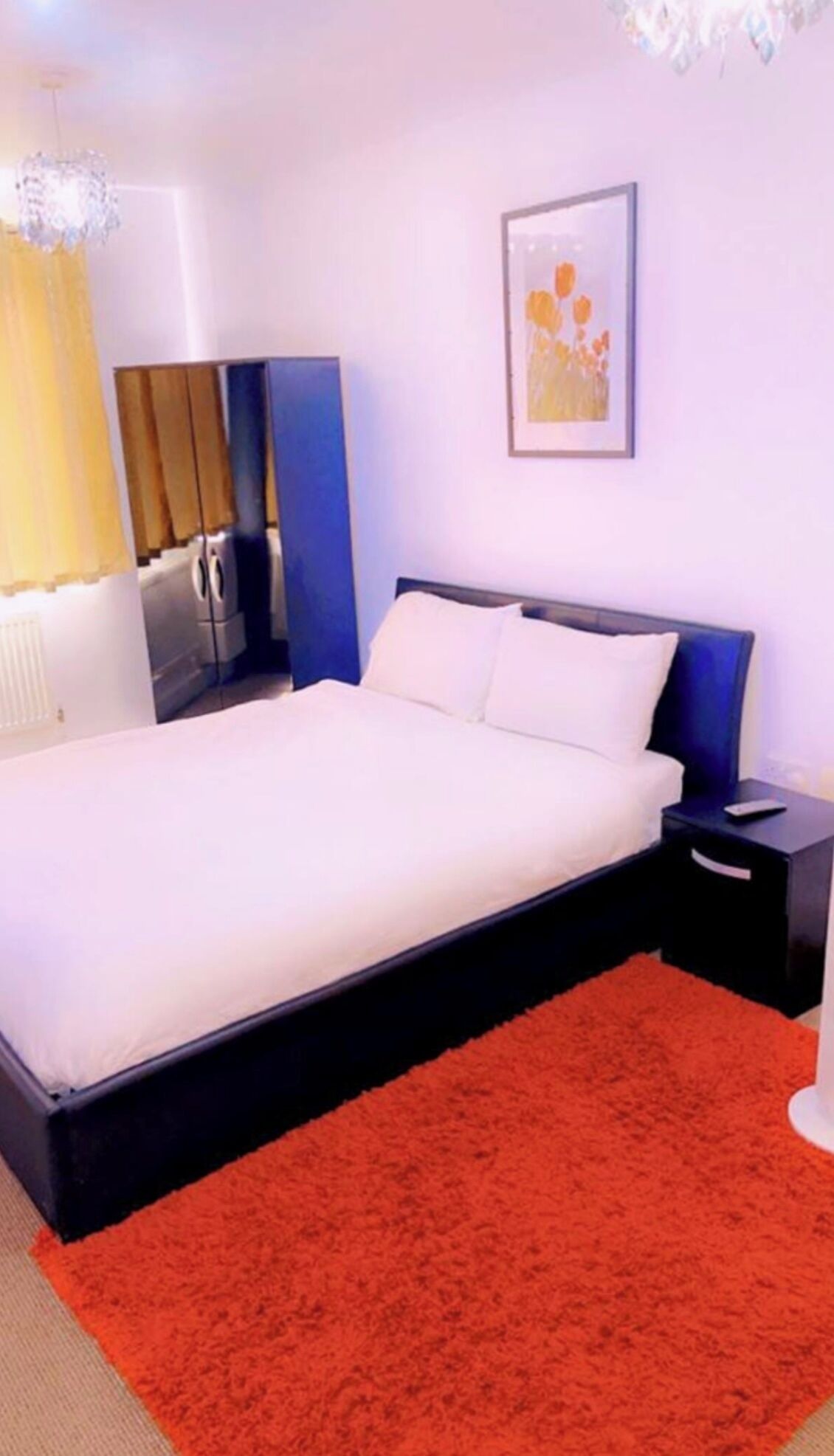 Een slaapkamer met een bed, nachtkastje, lamp en een schilderij aan de muur.
