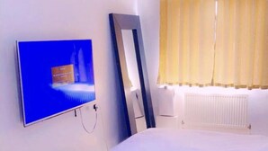 A hotel room with a bed, a television mounted on the wall, a mirror, and a window with curtains.