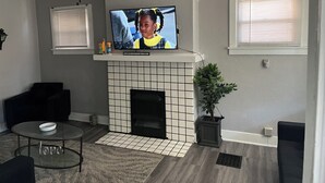 A living room with a fireplace, a ceiling fan, a television, and a potted plant. - Charming 3-bedroom house with AC and WiFi in lovely Pittsburgh (Pittsburgh)