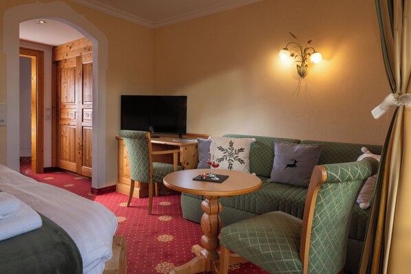 A hotel room with a bed, a green sofa, a wooden desk, a television, and a wall-mounted light fixture. - Hotel Sonnhof (Muehlbach Am Hochkoenig)