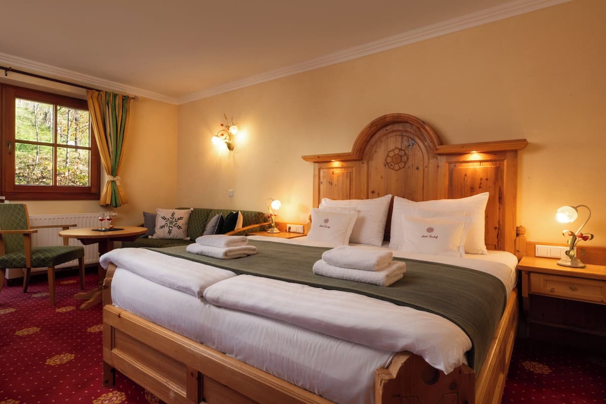 Une chambre d’hôtel avec un grand lit, une tête de lit en bois, deux tables de chevet avec des lampes, une chaise et une fenêtre avec des rideaux.