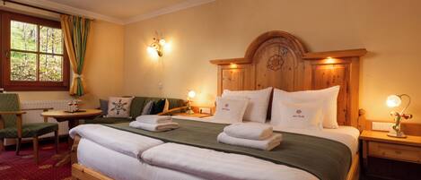A hotel room with a large bed, a wooden headboard, two bedside tables with lamps, a chair, and a window with curtains.