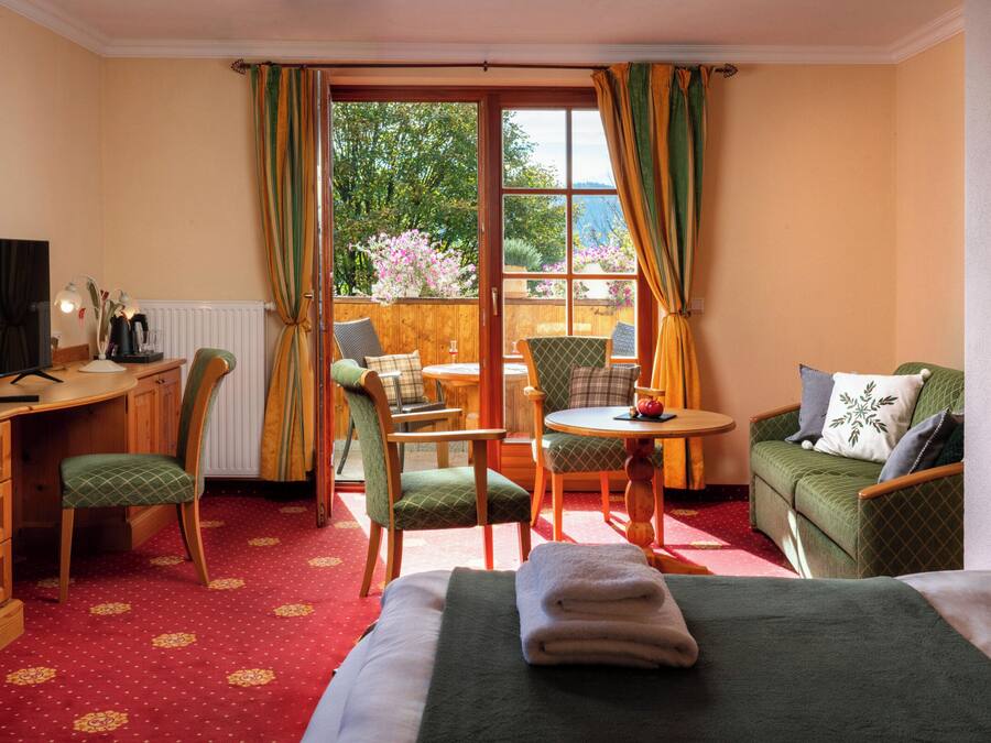 A hotel room with a bed, a desk with a computer, a chair, a small table, and a sofa. There is a window with curtains, and a view of the outdoors.