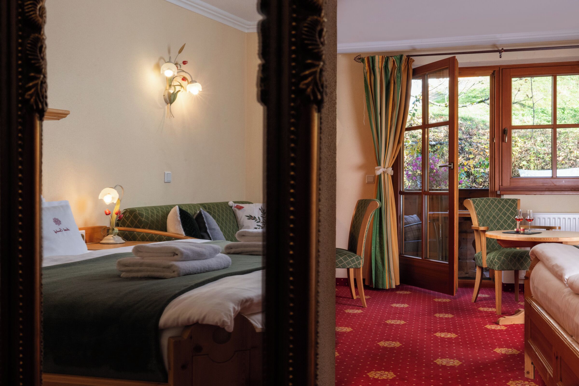 A hotel room with a bed, a chair, a table with a glass, and a window with curtains.