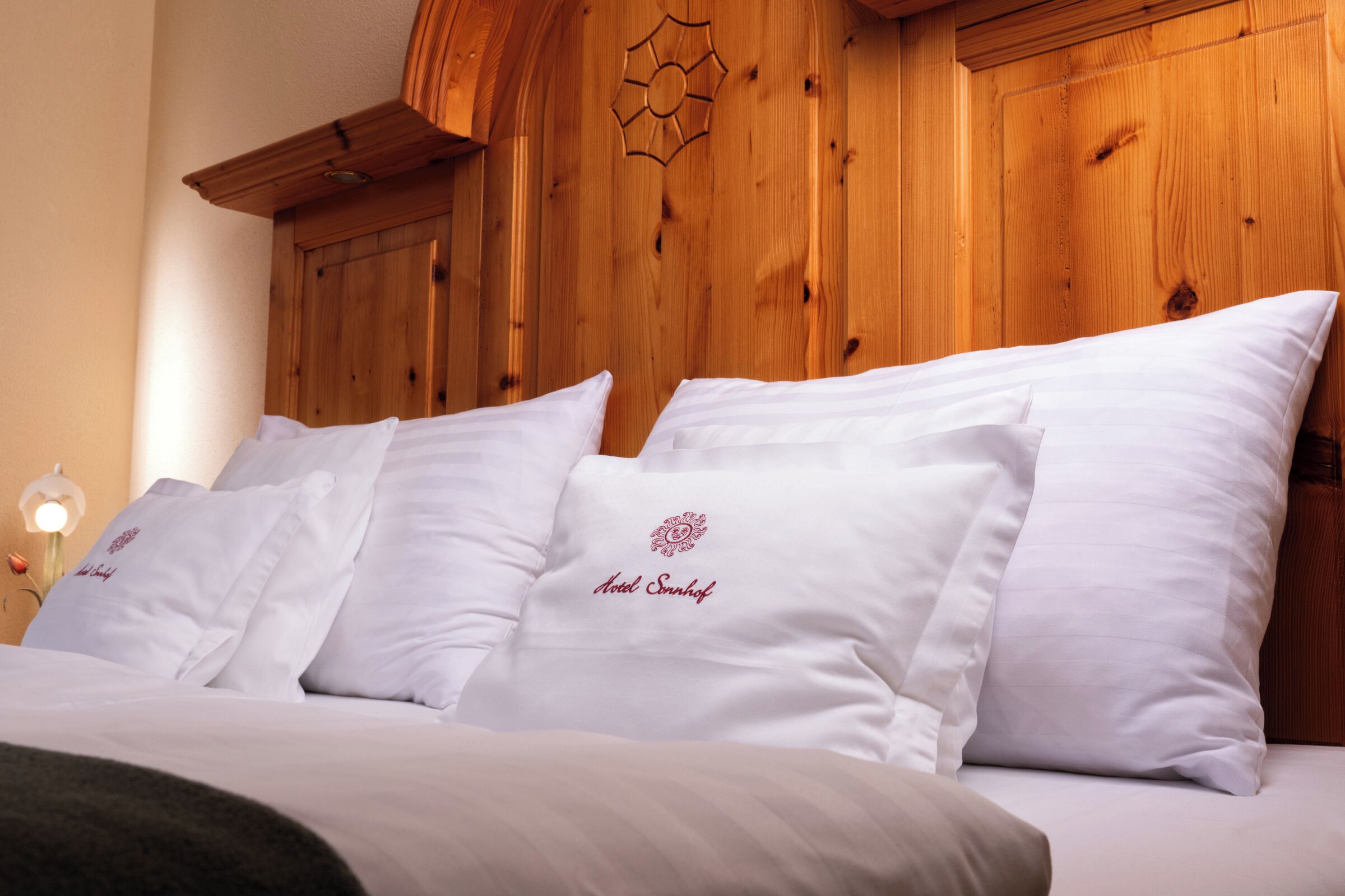 A bed with white linens and pillows, a wooden headboard, and a decorative wall piece.
