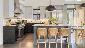 A modern kitchen with dark cabinetry, stainless steel appliances, a central island with bar stools, and pendant lighting. - Sundrenched by Avantstay Pool, Mins to Old Town (Scottsdale)