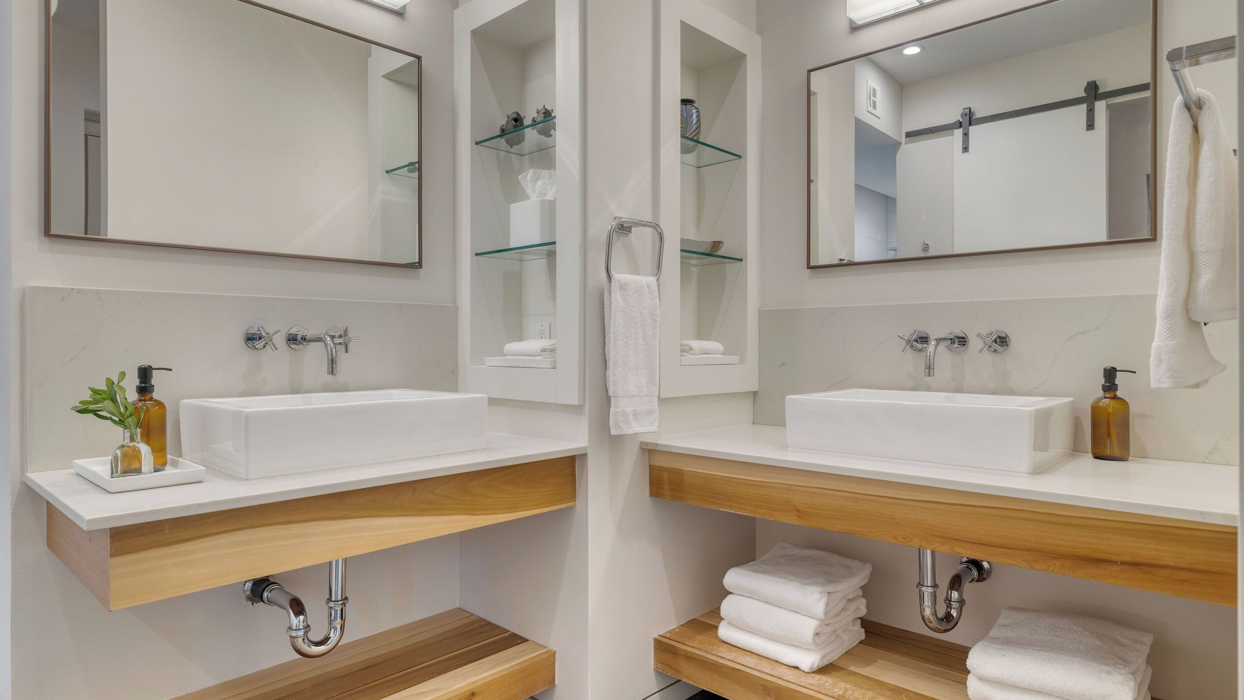 A modern bathroom with two sinks, mirrors, and wooden shelves.