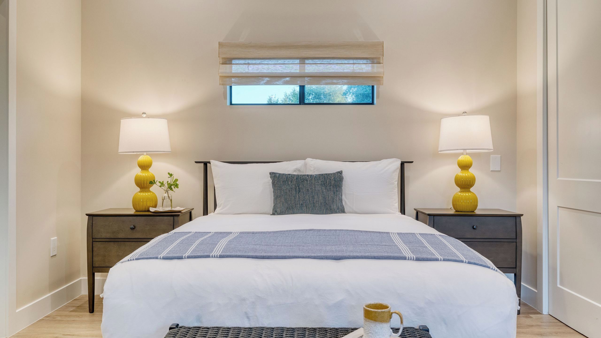 A hotel room with a bed, two bedside tables with lamps, a window, and a bedside plant.
