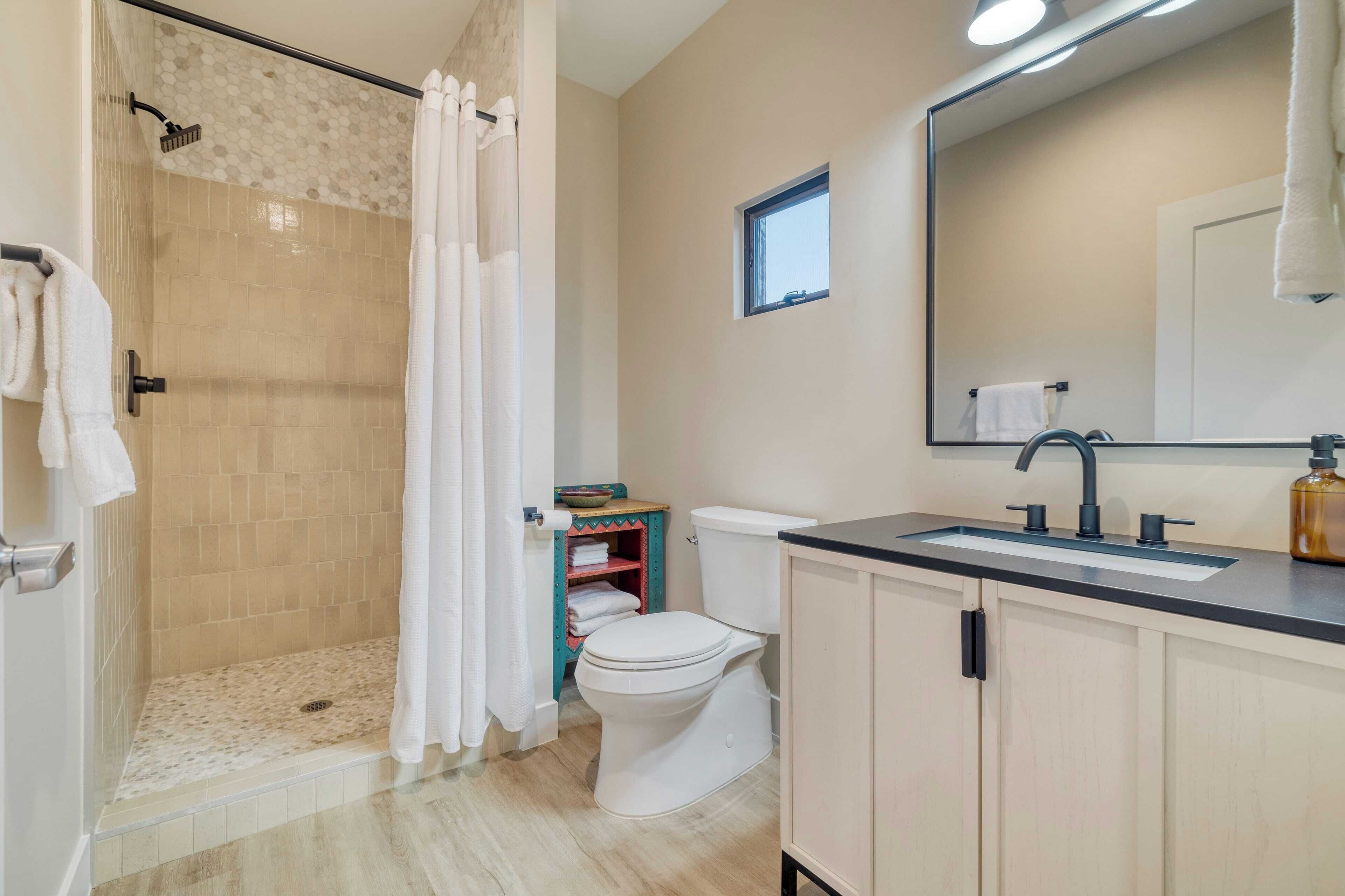A bathroom with a shower, toilet, sink, and a mirror.