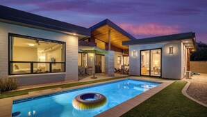 A modern house with a swimming pool, a covered patio, and a well-lit interior. - Sundrenched by Avantstay Pool, Mins to Old Town (Scottsdale)