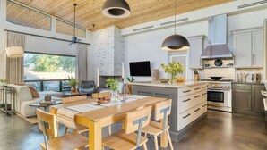 A modern kitchen with a central island, a dining area with wooden furniture, and a living space with a sofa and a TV. - Sundrenched by Avantstay Pool, Mins to Old Town (Scottsdale)