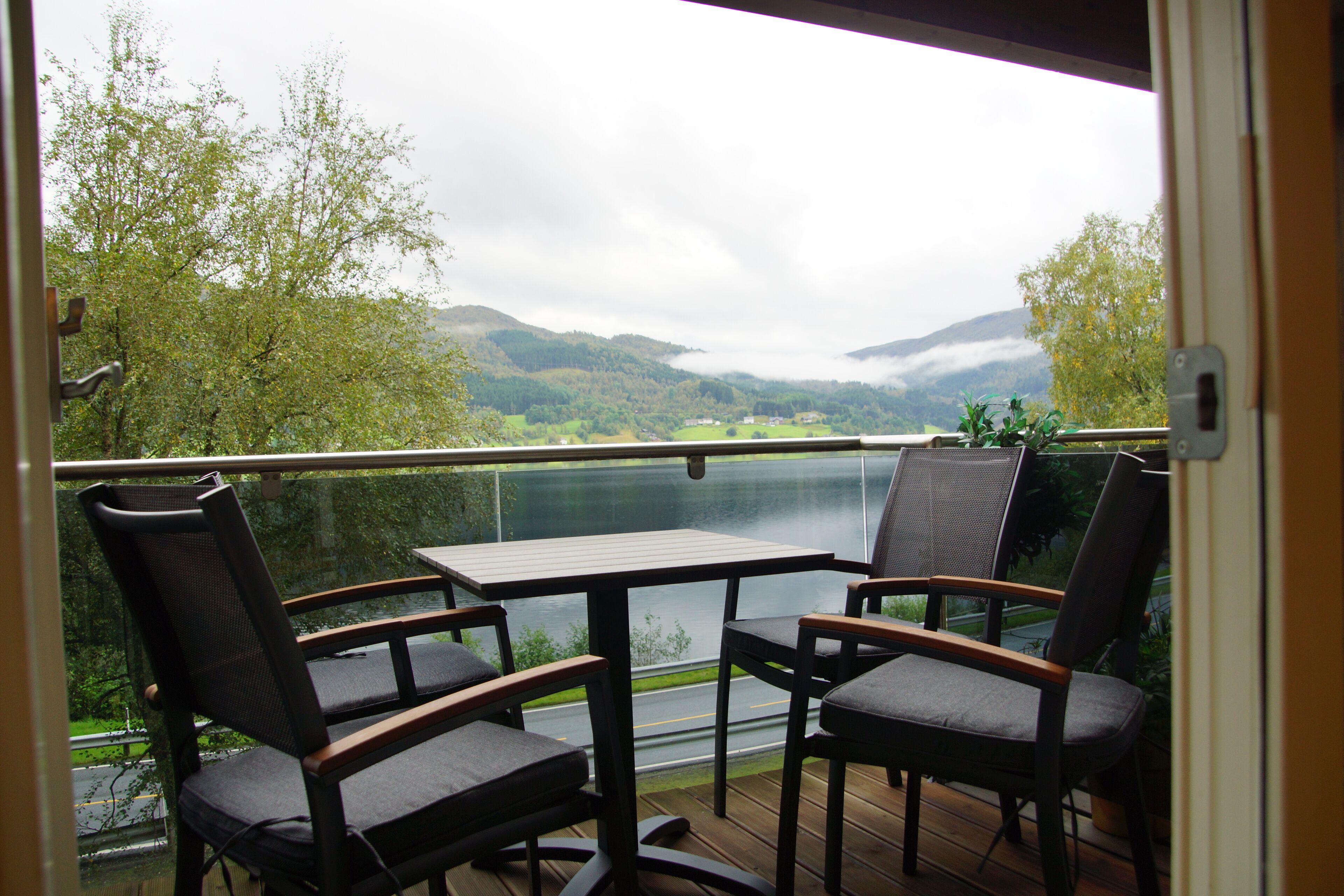 Un balcon avec une table et deux chaises, donnant sur un lac et des montagnes.