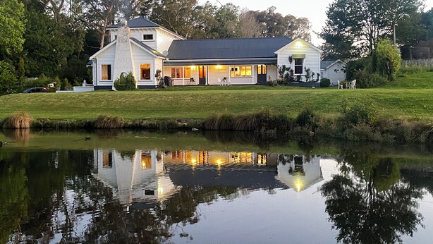 A two-story house with a large porch and a pond in front. - Modernized country house set in beautiful gardens with swimming pool.  
 (Rangitumau)