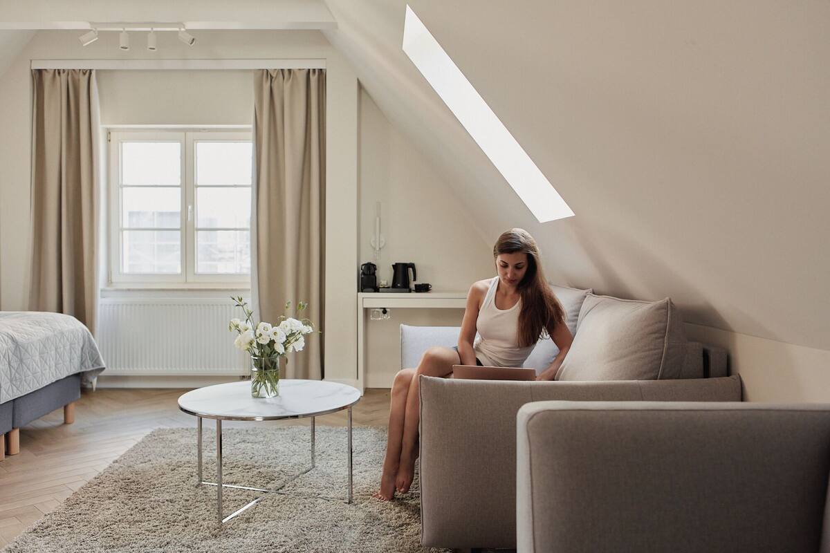 A modern loft bedroom with a sloped ceiling, a bed, a sofa, a small round table, and a window with curtains.