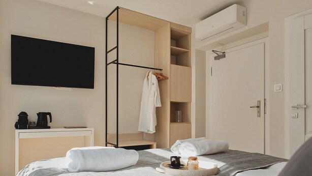 A hotel room with a bed, a TV, a wardrobe, a desk with a coffee maker, and a shelf with a robe and a mug. - Stągiewna Residence by Downtown Apartments (Gdansk)