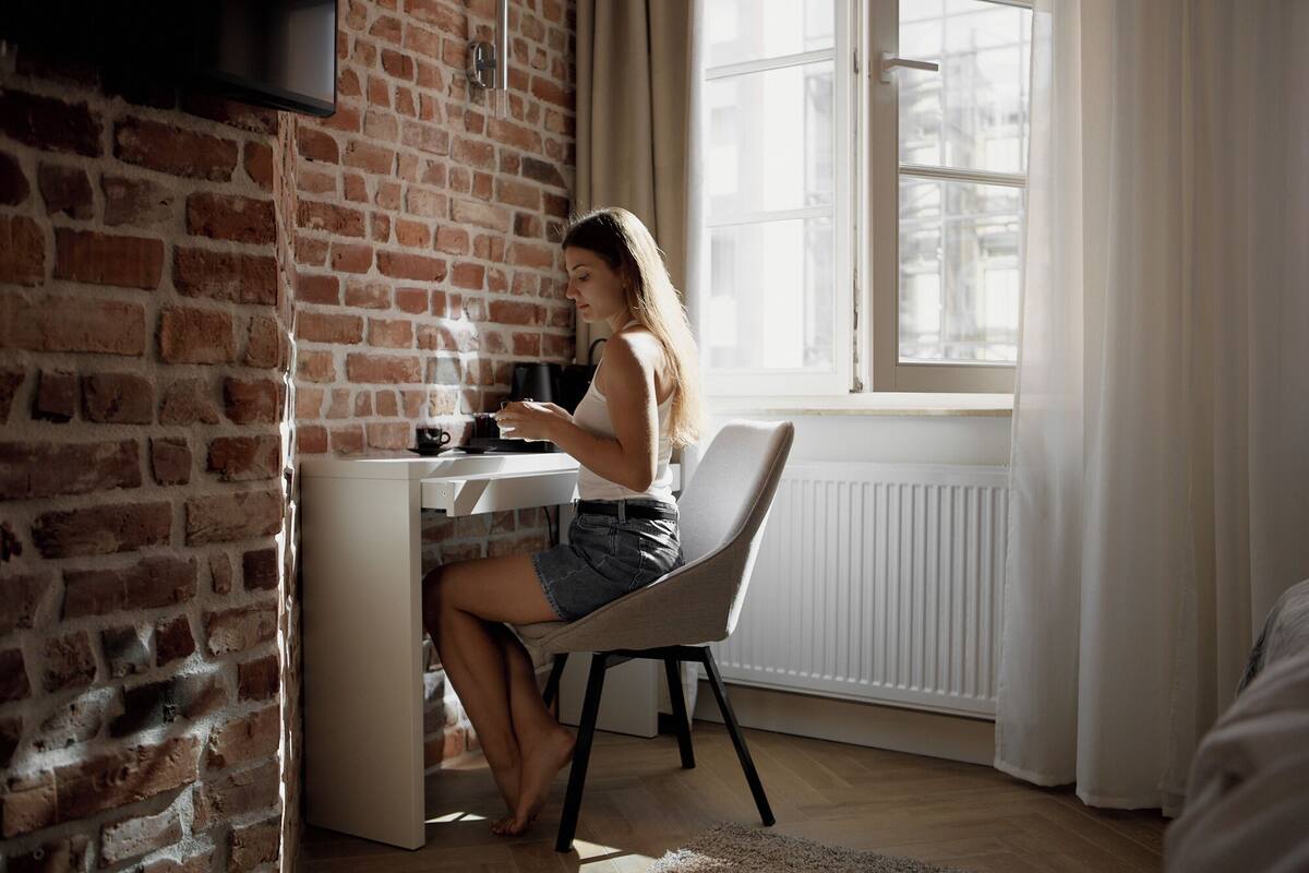 A person sitting at a desk in a room with a brick wall and a window.