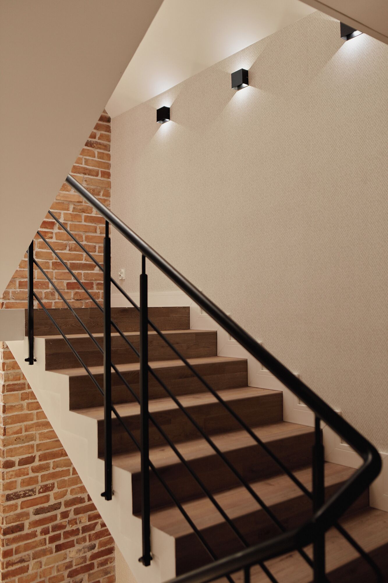 A staircase with a brick wall on one side and a textured wall on the other, featuring a black metal railing.