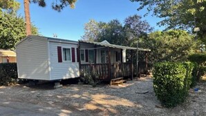 A mobile home with a porch and a small deck, surrounded by trees and a gravel driveway.