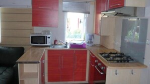 A compact kitchen with red cabinets, a microwave, a coffee maker, and a gas stove.