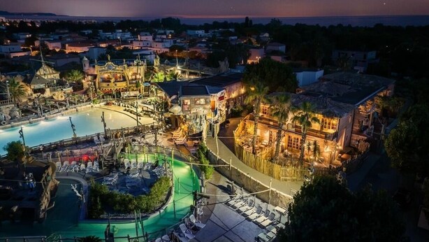 A resort with a swimming pool, outdoor seating, and a well-lit building.
