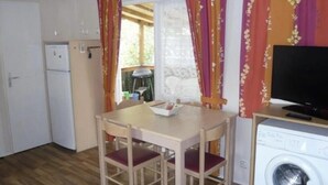 A compact kitchen with a dining table, chairs, a washing machine, and a television on a wooden stand.