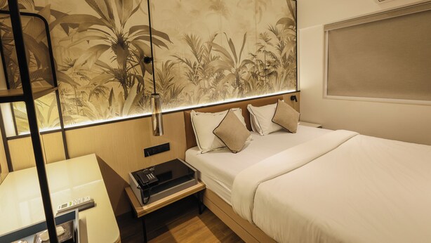A hotel room with a bed, bedside table, lamp, and a large wall mural. - Hotel Western (Mumbai)