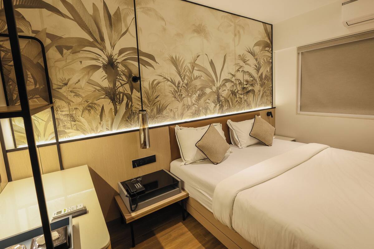 A hotel room with a bed, bedside table, lamp, and a large wall mural.
