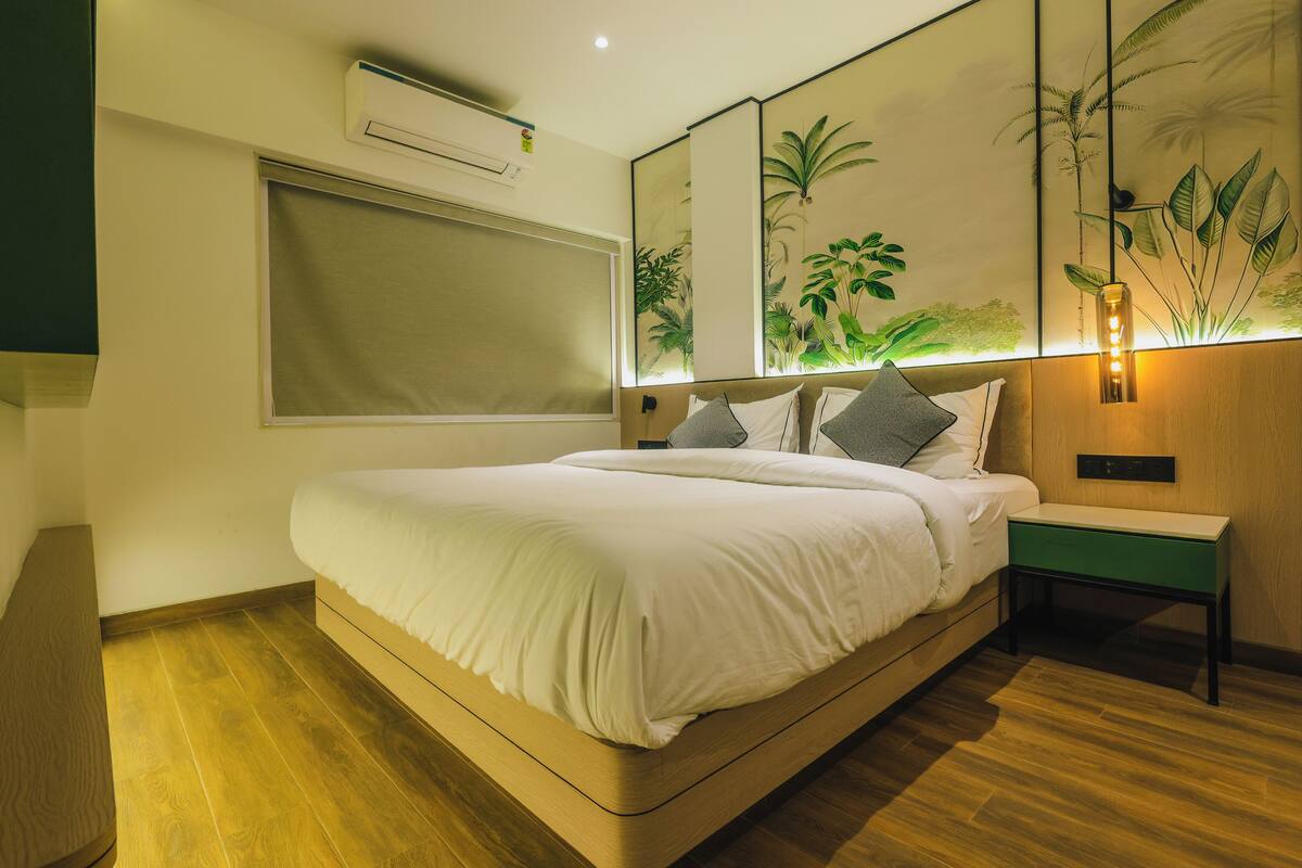 A modern bedroom with a large bed, a bedside table, a wall-mounted air conditioner, and a large window.