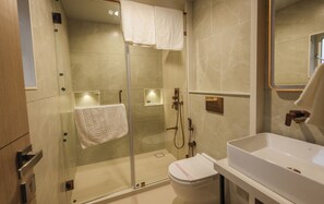 Enjoy a refreshing shower with a handheld showerhead and wall-mounted control panel, alongside a toilet and spacious sink area.