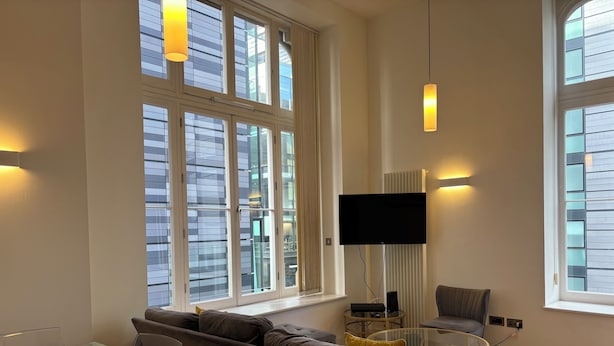 Een moderne woonkamer met een glazen tafel, een bank, een televisie en grote ramen.
