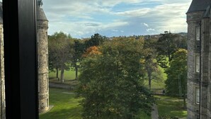 Uitzicht op een historisch gebouw met een toren en een stenen muur, omringd door bomen en een gazon.