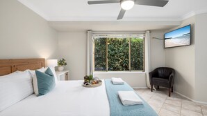 Ein Schlafzimmer mit einem Bett, einem Nachttisch, einem Sessel, einem Fenster mit Aussicht und einem Deckenventilator.