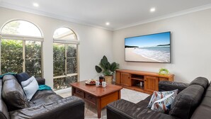 Ein Wohnzimmer mit Ledersofas, einem Holztisch und einem großen Fernseher, der eine Strandansicht zeigt.