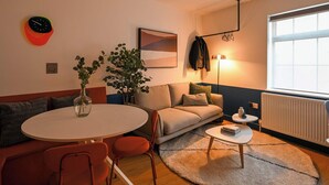 Un salon chaleureux avec une table à manger ronde, un canapé et une table basse. On y trouve une plante, une horloge et un tableau encadré accroché au mur.