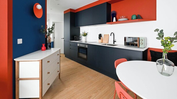 Une cuisine moderne avec un plan de travail blanc, des armoires noires et un mur d’accent rouge.