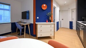 Une cuisine moderne dotée d’un four encastré, un coin repas avec une table et des chaises, et un téléviseur fixé au mur.