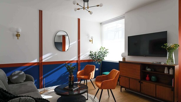 A modern living room with a sofa, two orange chairs, a round coffee table, a TV, and a bookshelf.